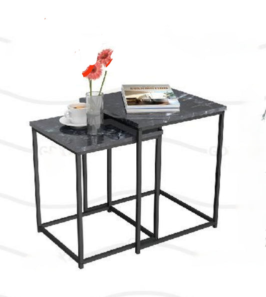A black rectangular coffee table with a steel frame, featuring a flat pack assembly needed label, with a glass cup and a red flower on top.